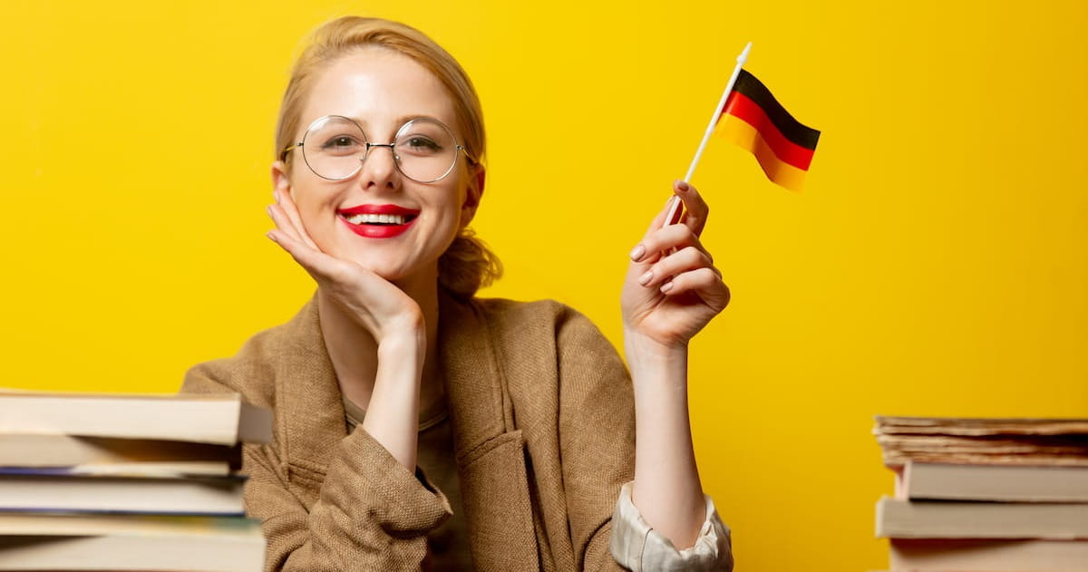 Smiling woman holding the German flag with books around her.