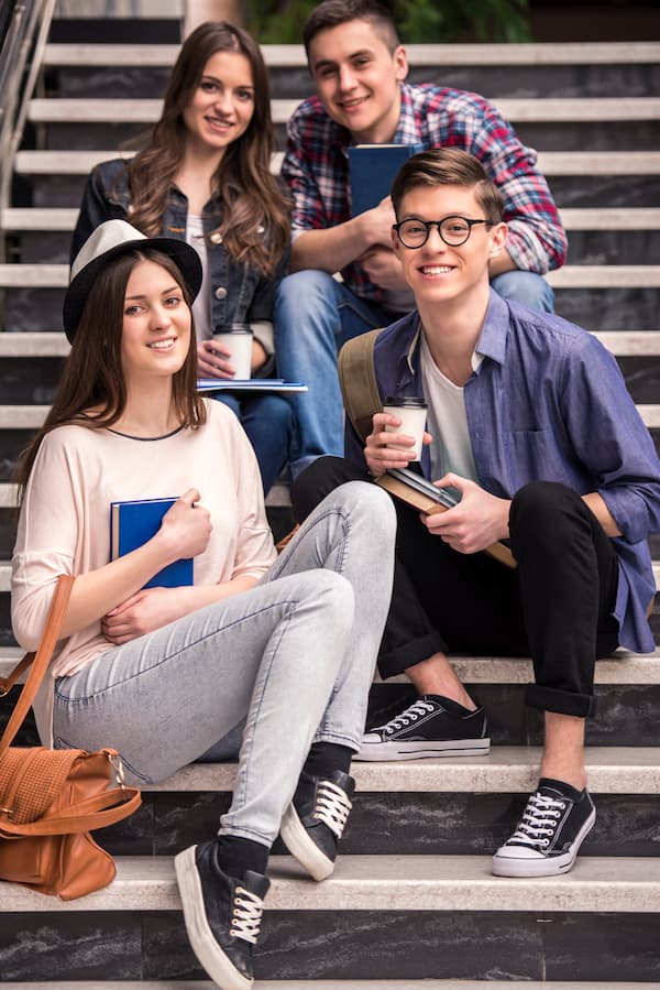4 Students Sitting On The Stairs And Smiling